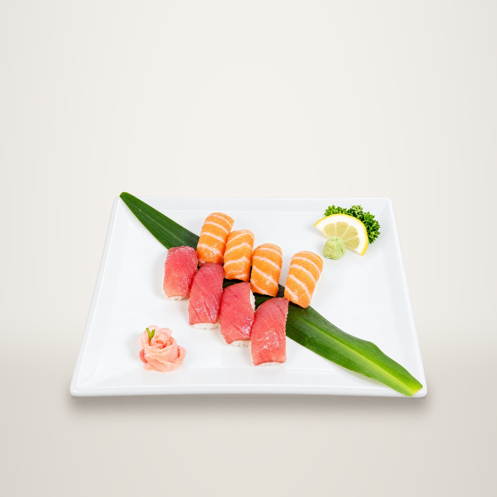 Assiette blanche garnie de quatre nigiris au saumon et de quatre au thon, posés sur une feuille verte avec gingembre mariné et rondelle de citron.