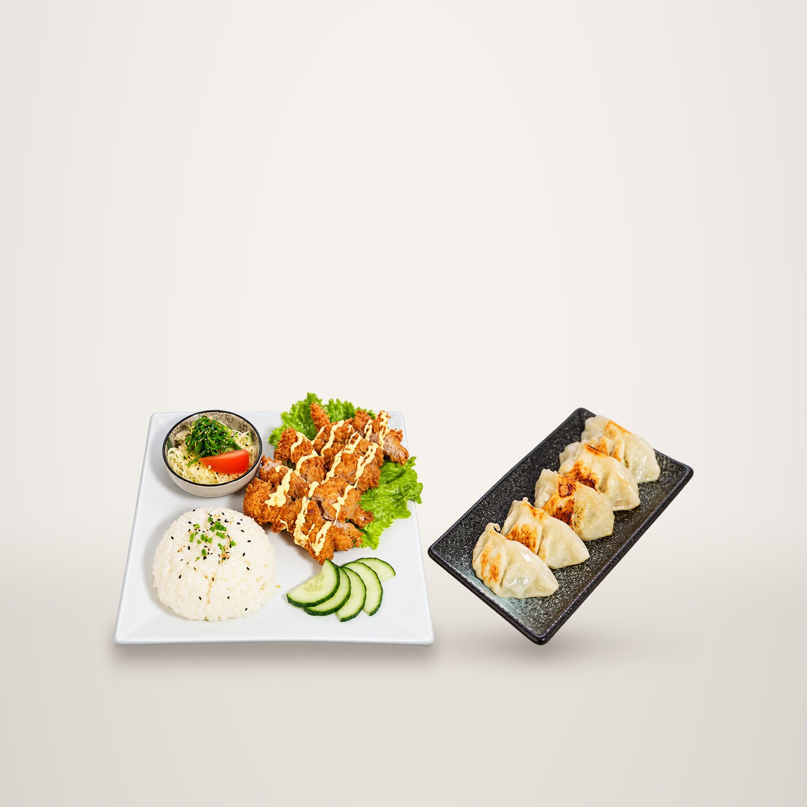 Une assiette blanche de poulet pané nappé de sauce avec riz, salade et concombre, à côté d'un plateau noir de gyozas grillés.