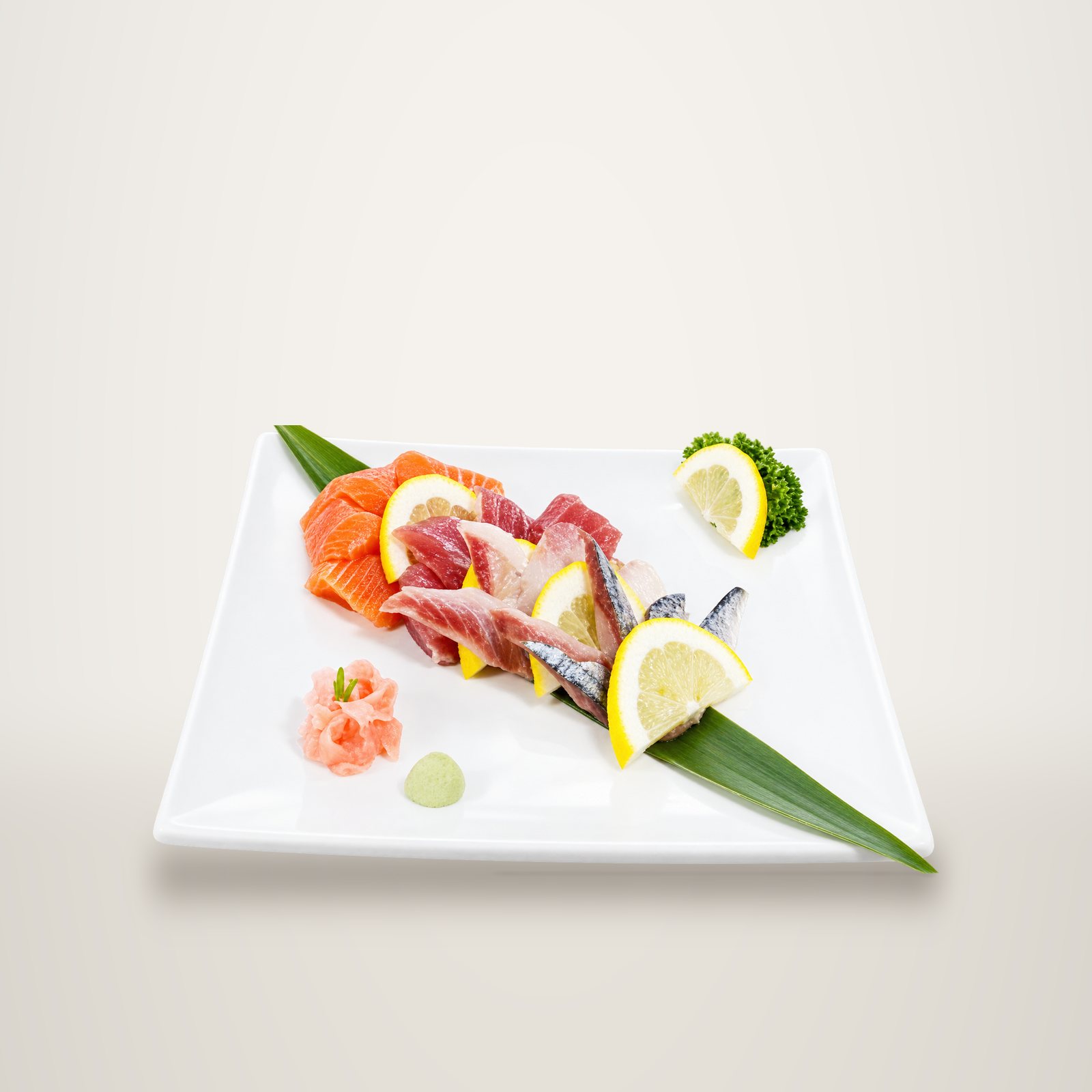 Assiette blanche garnie de tranches de saumon, thon et autres poissons crus, accompagnés de rondelles de citron, de gingembre et de wasabi sur une feuille verte.