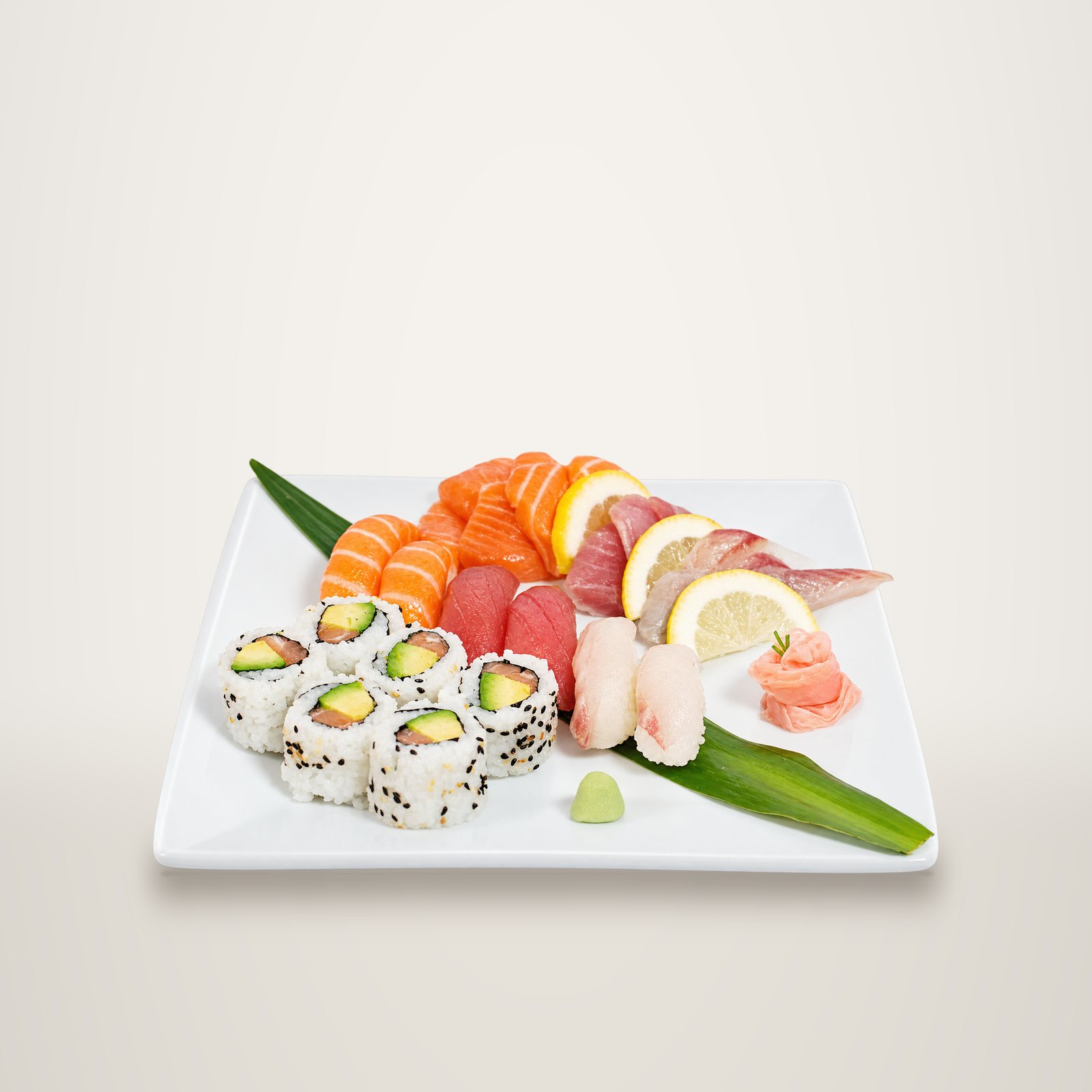Assiette blanche garnie de makis à l'avocat, de sushis et sashimis de saumon, thon et poisson blanc, avec citron, gingembre et wasabi.