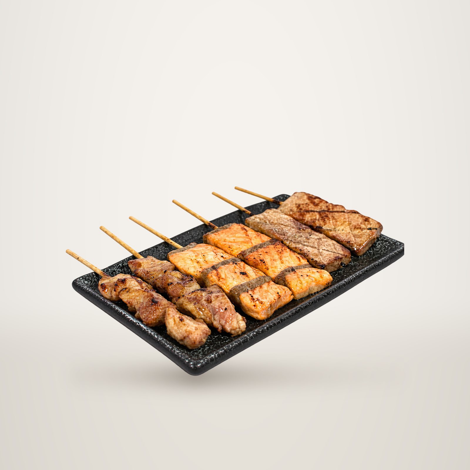 Plateau noir en céramique présentant des brochettes grillées de viande, de saumon et de thon sur fond blanc.