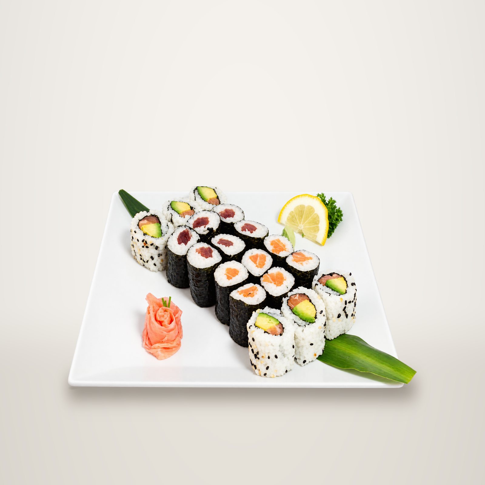 Plateau blanc garni de makis au thon et au saumon, de california rolls à l'avocat, de gingembre mariné en forme de rose et d'une tranche de citron.