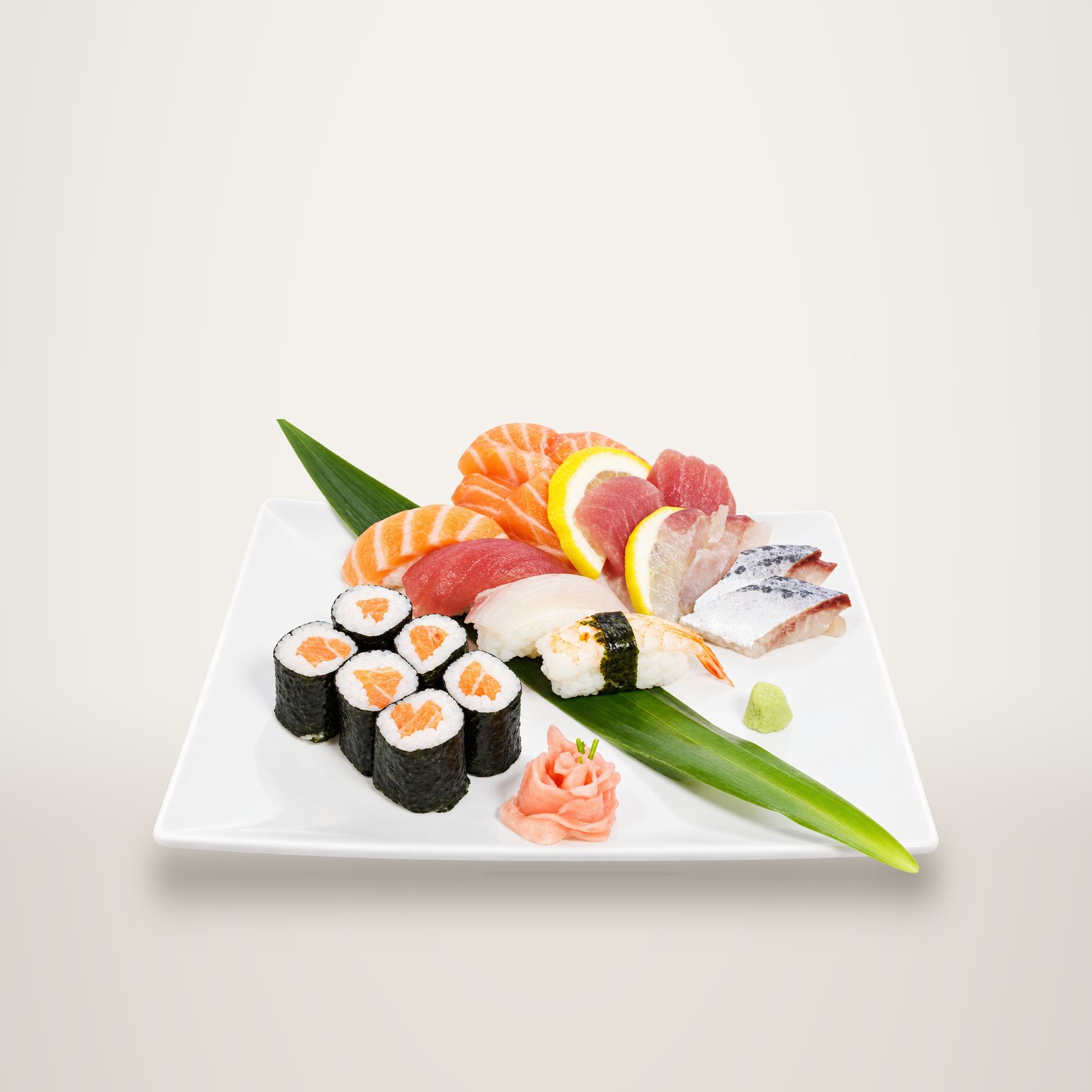 Assiette blanche garnie de makis au saumon, de nigiris, de tranches de sashimi, de citron, de gingembre et de wasabi sur une feuille verte.