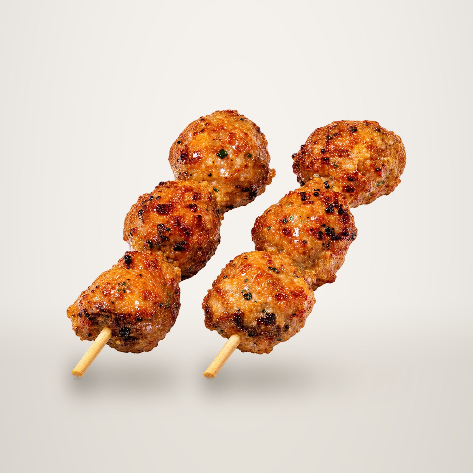Deux brochettes en bois garnies de boulettes de viande dorées et grillées, présentées sur un fond blanc uni.