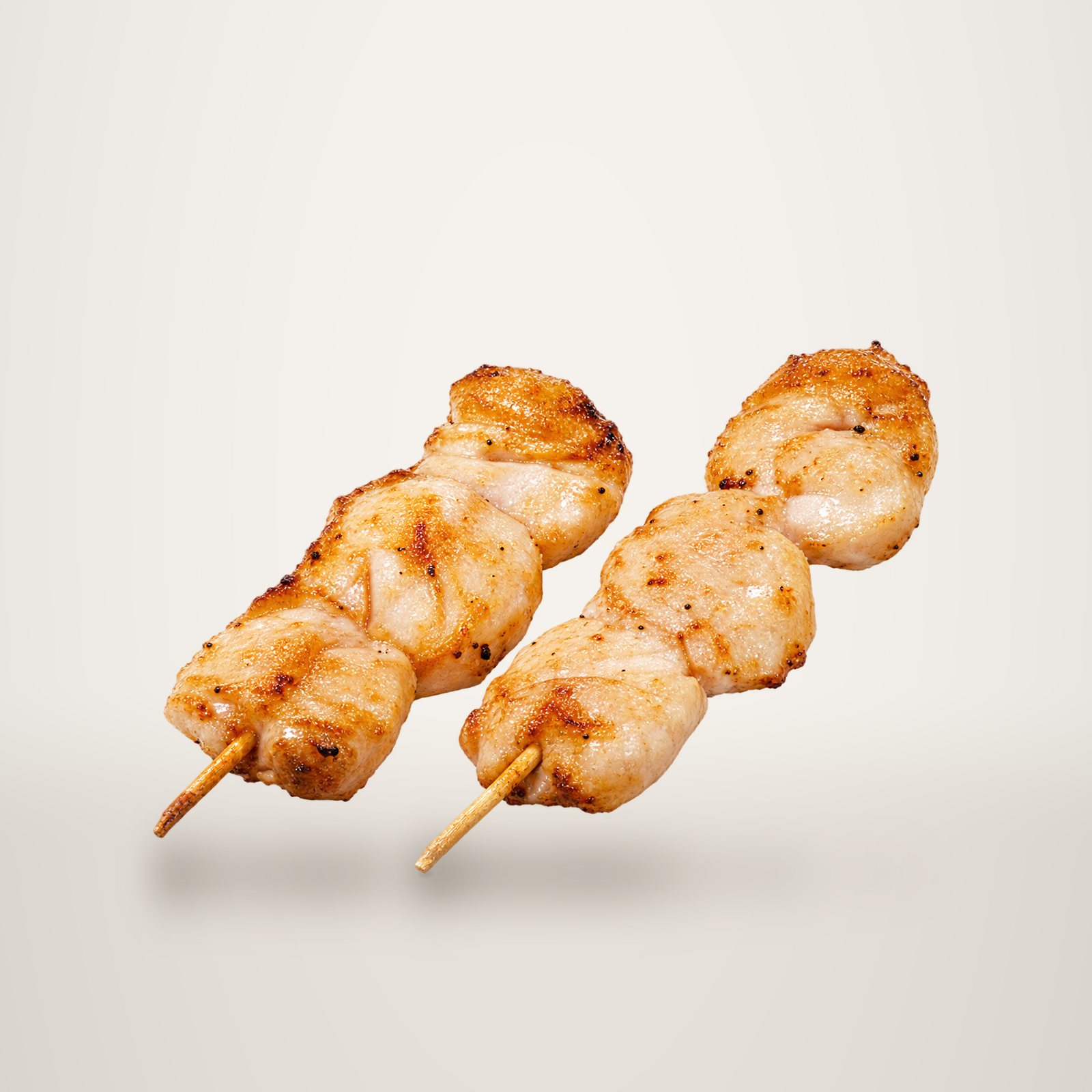 Deux brochettes de morceaux de poulet grillé sur des piques en bois, photographiées sur fond blanc.