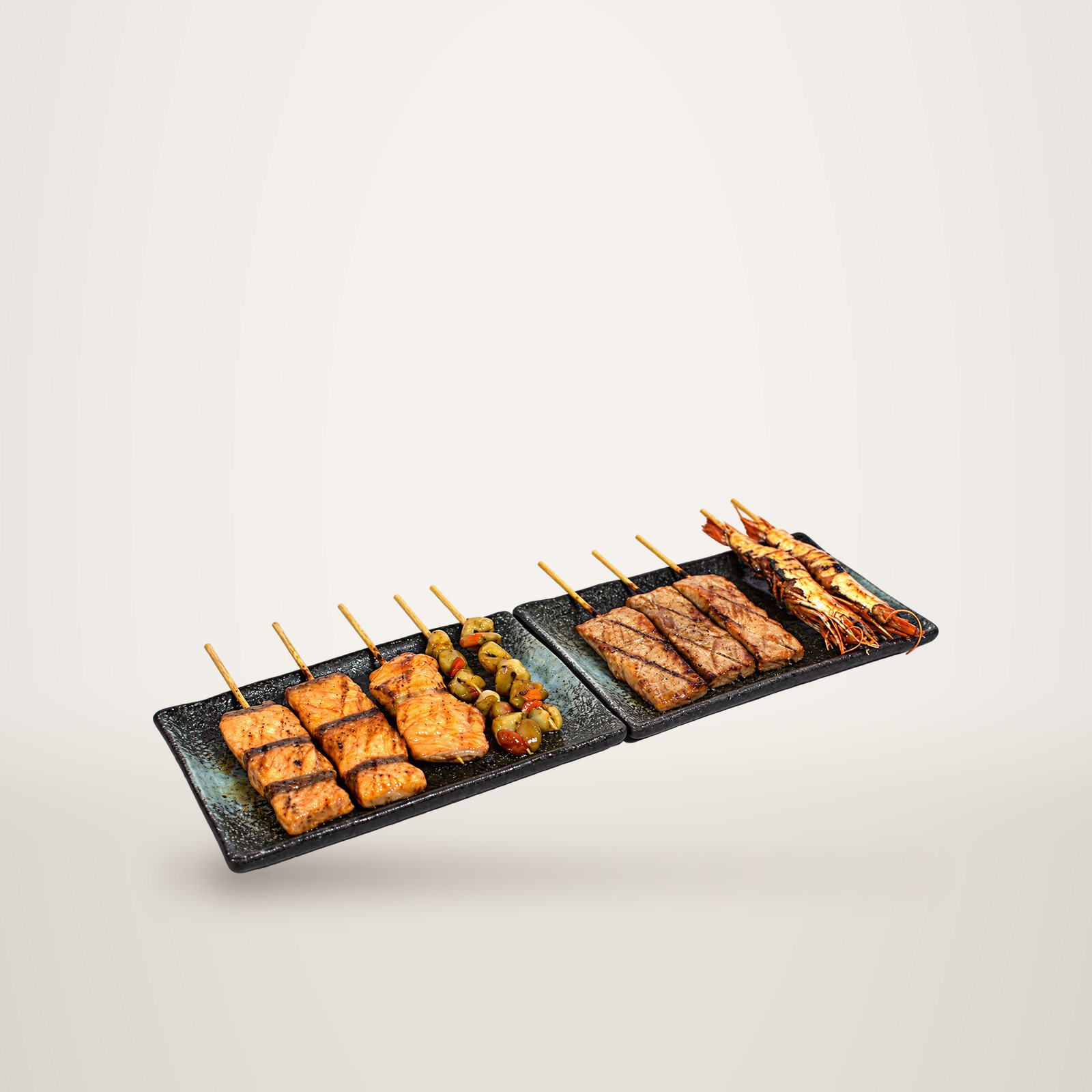 Deux assiettes noires en céramique présentent des brochettes grillées de saumon, de légumes, de thon et de grosses crevettes sur fond blanc.