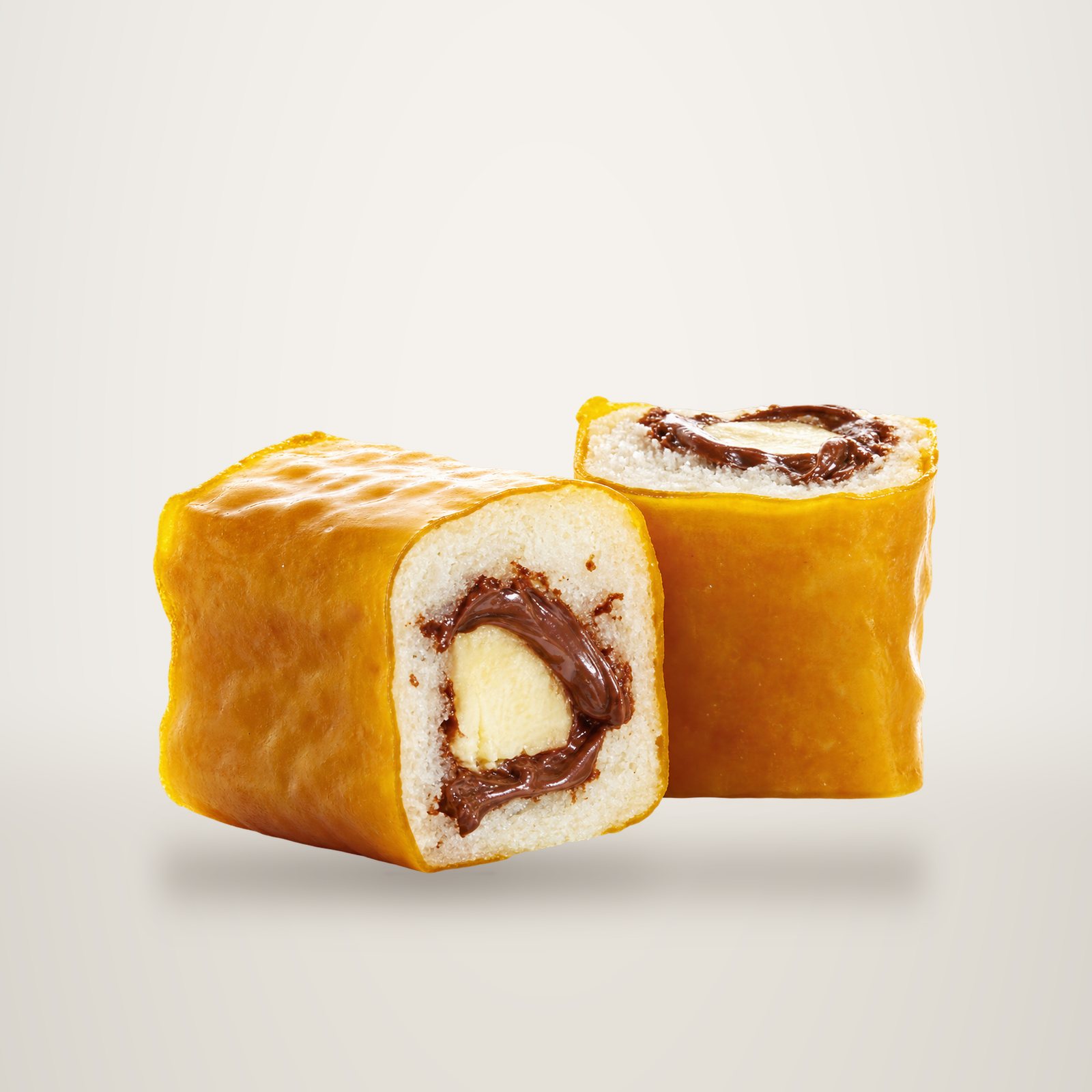 Deux morceaux de maki sucré enrobés d'une fine couche jaune, garnis de riz, de banane et de pâte au chocolat, présentés sur fond blanc.