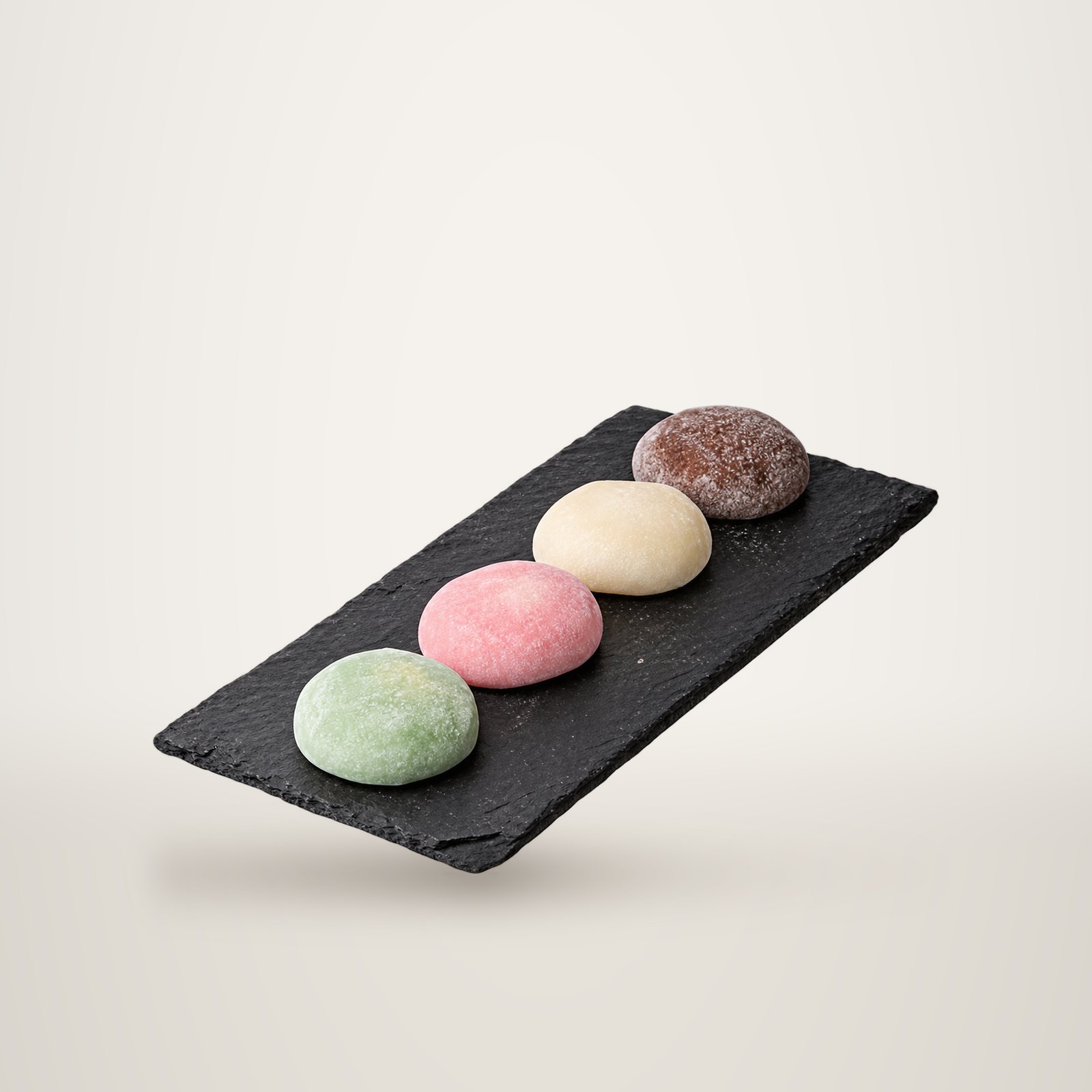 Quatre mochis vert, rose, blanc et brun disposés en ligne sur une ardoise noire, sur fond blanc.